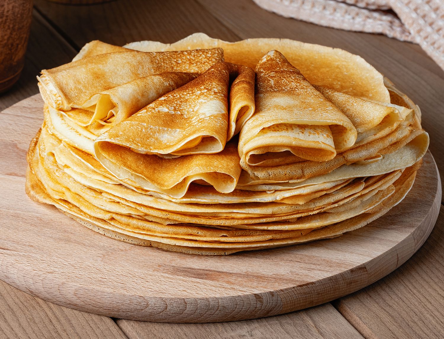 Pila di crêpes dorate arrotolate su un tagliere di legno