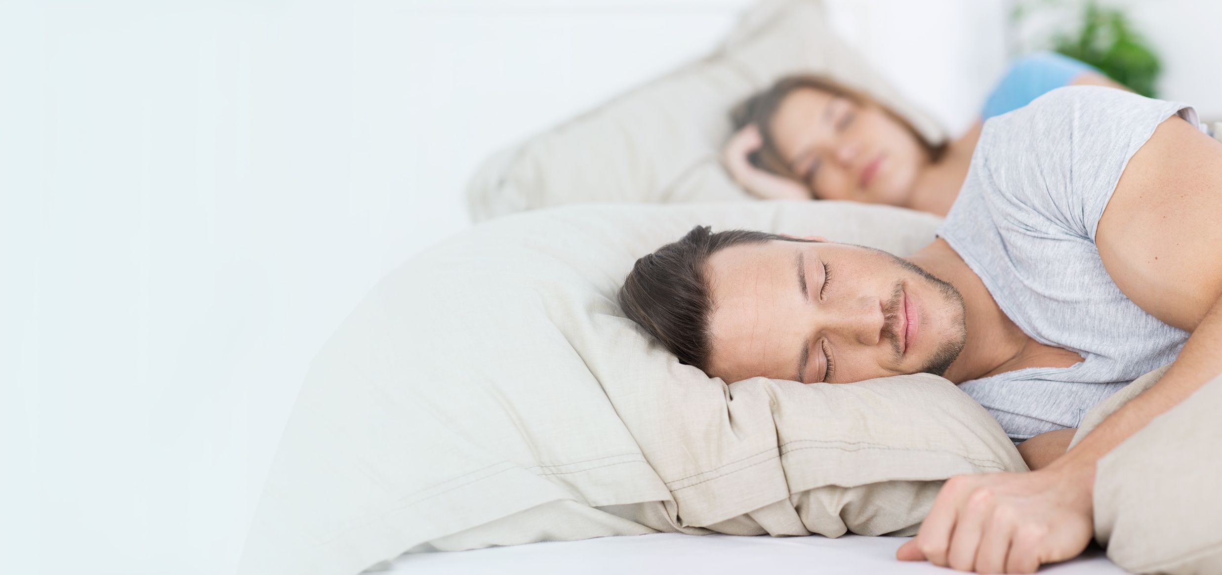 Coppia che dorme serenamente in un letto con lenzuola chiare, ripresa di profilo, ambiente luminoso
