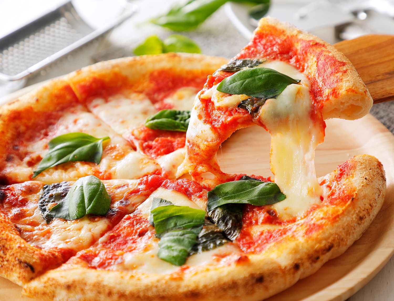 Fetta di pizza margherita filante sollevata con una paletta di legno, con foglie di basilico sopra