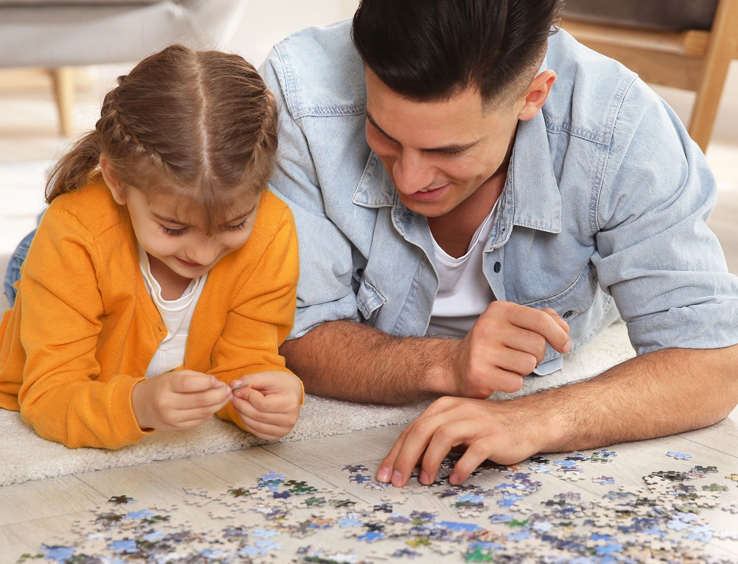 Padre e figlia sdraiati a pancia in giù sul pavimento mentre montano insieme un puzzle