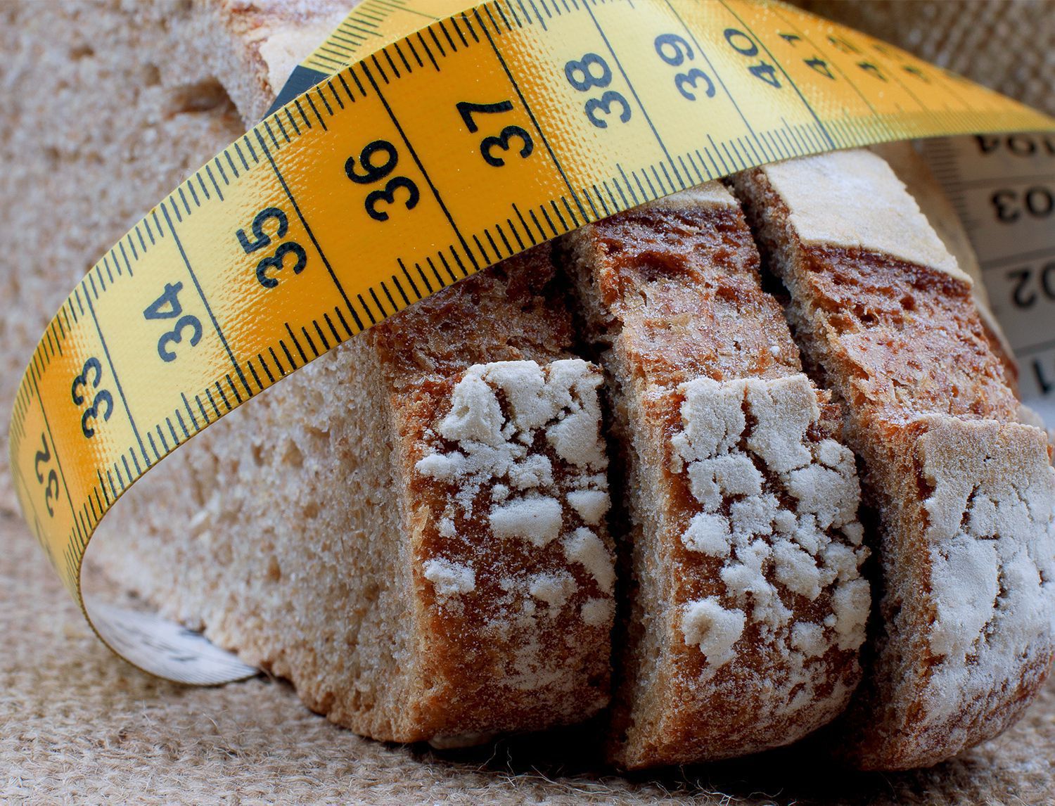 Fetta di pane integrale a fette con un metro da sarto arrotolato sopra, sfondo di tela di iuta