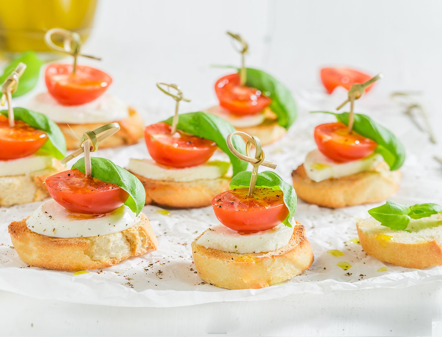 Crostini con mozzarella, pomodorino e basilico infilzati con stuzzicadenti, disposti su carta forno