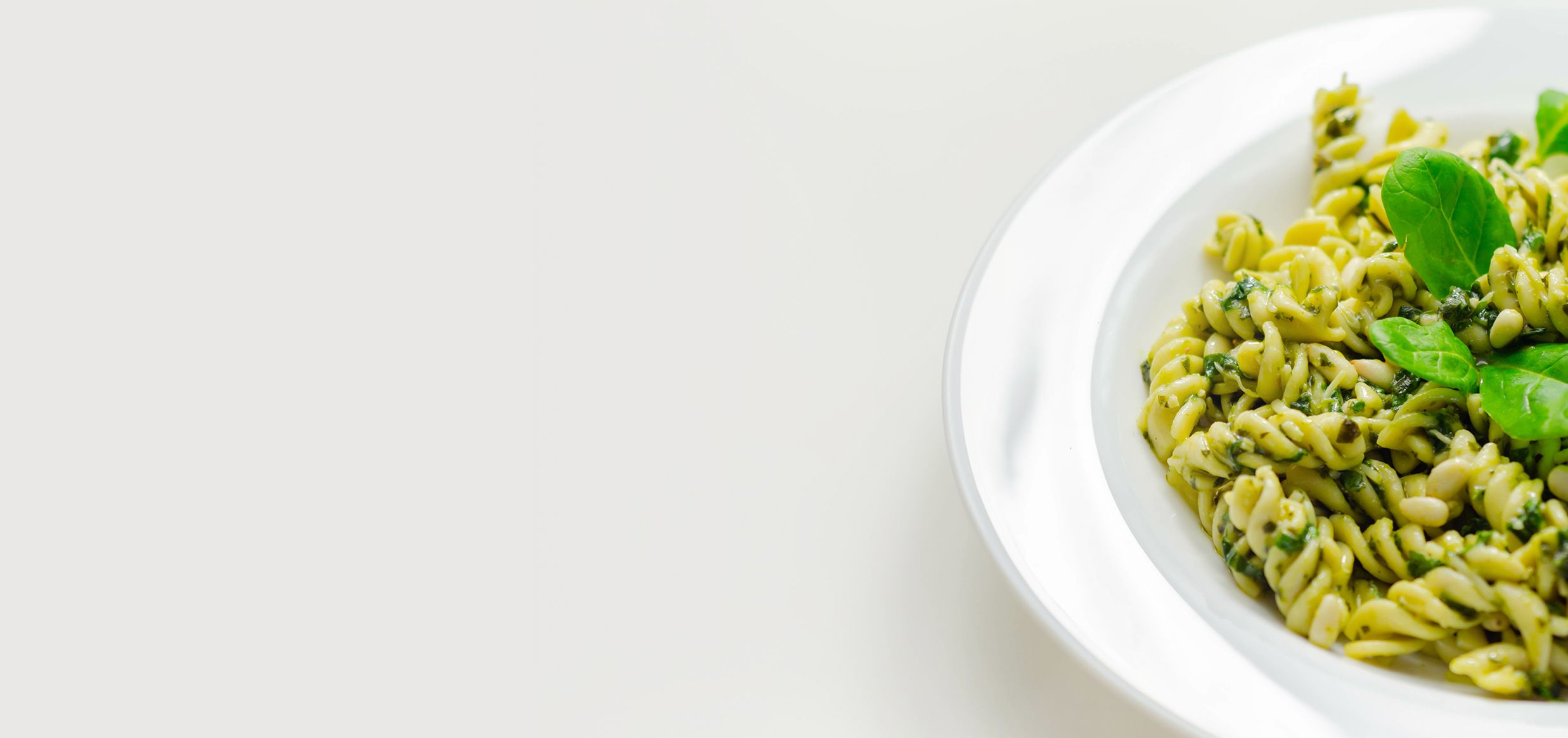 Piatto di fusilli conditi con pesto verde, pinoli e foglie di rucola, vista dall’alto