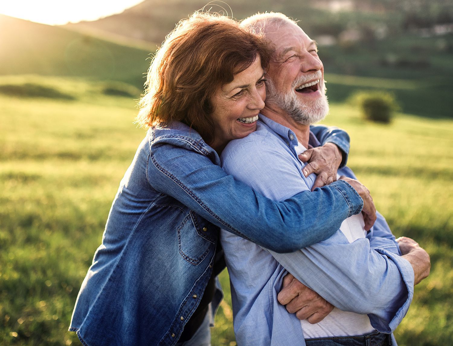 Coppia di anziani sorridenti che si abbracciano all'aperto, in un prato al tramonto