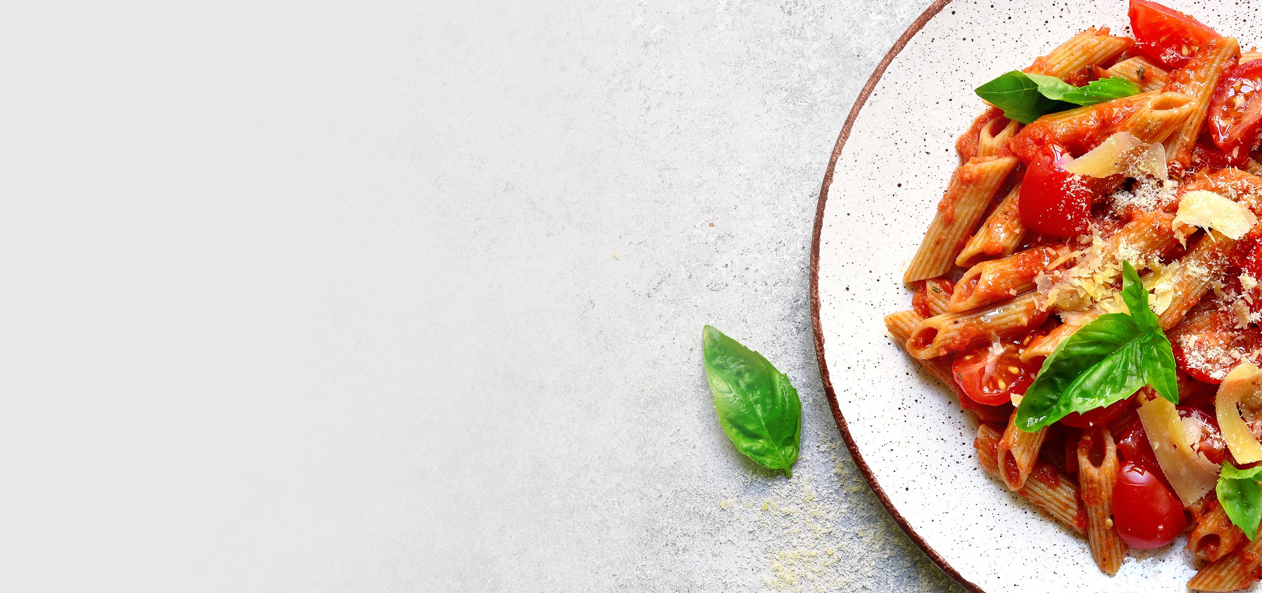Piatto di penne al pomodoro con pomodorini, scaglie di formaggio e foglie di basilico, vista dall’alto