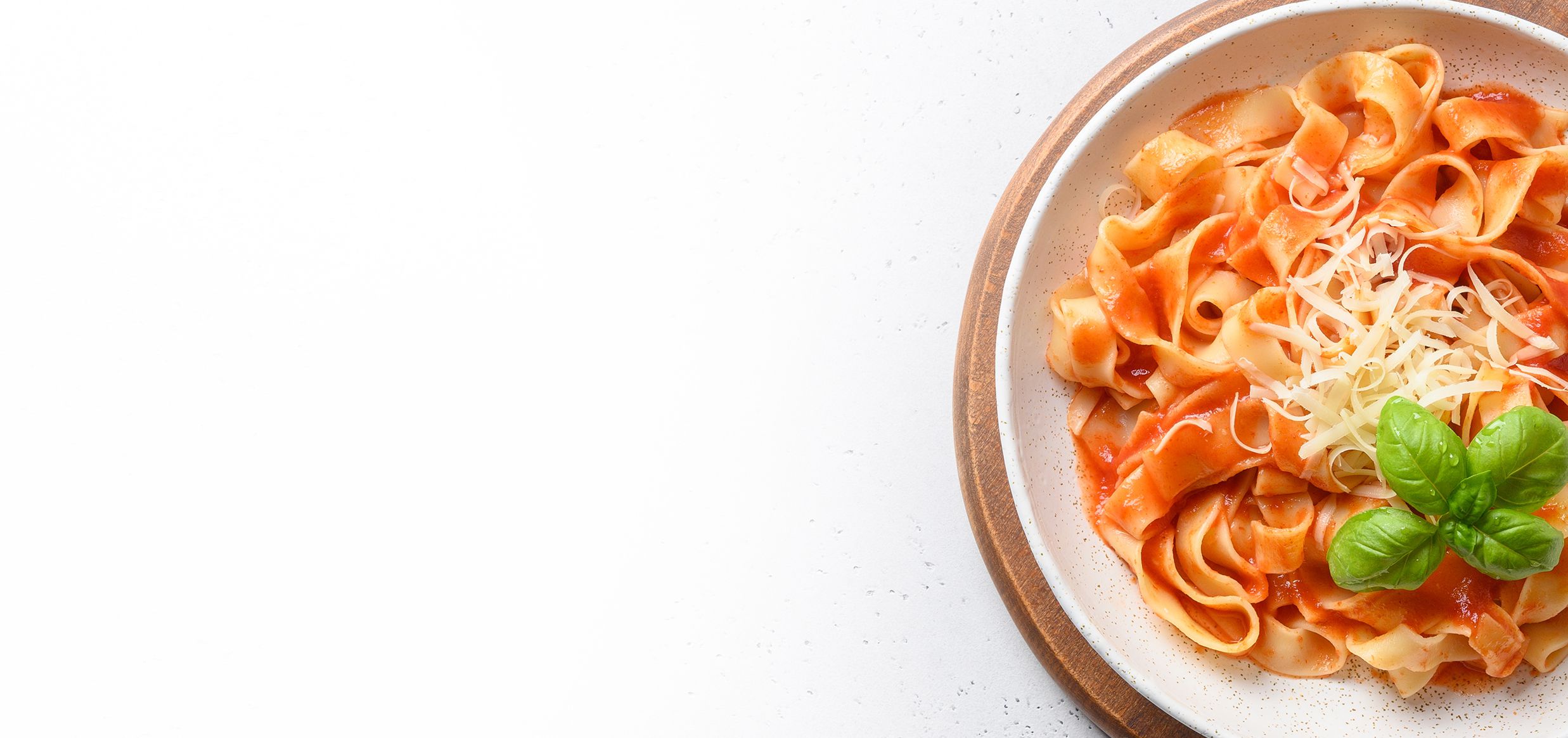 Piatto di fettuccine al pomodoro con scaglie di formaggio grattugiato e foglie di basilico, vista dall’alto