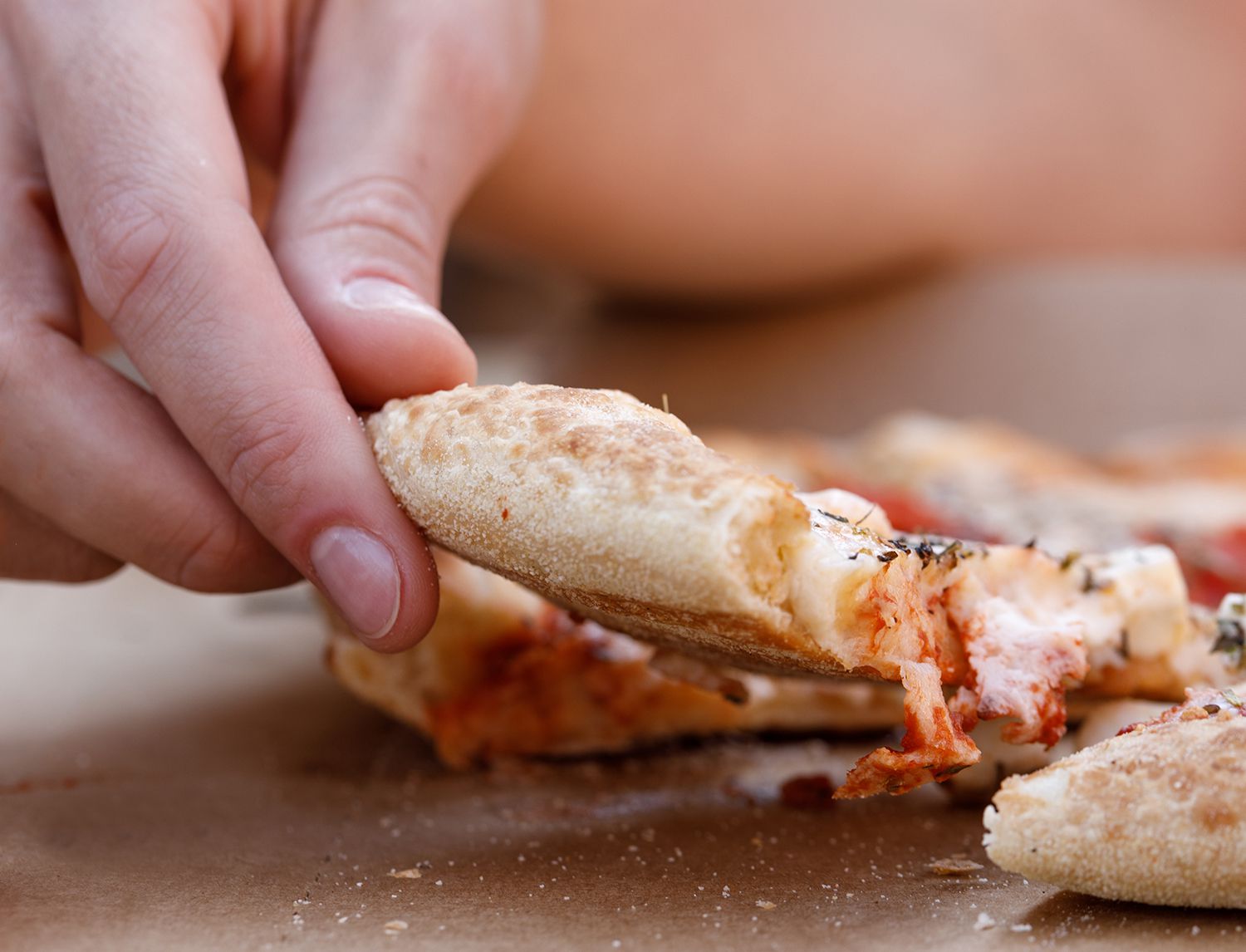 Primo piano di una mano che solleva una fetta di pizza al taglio, con la mozzarella filante