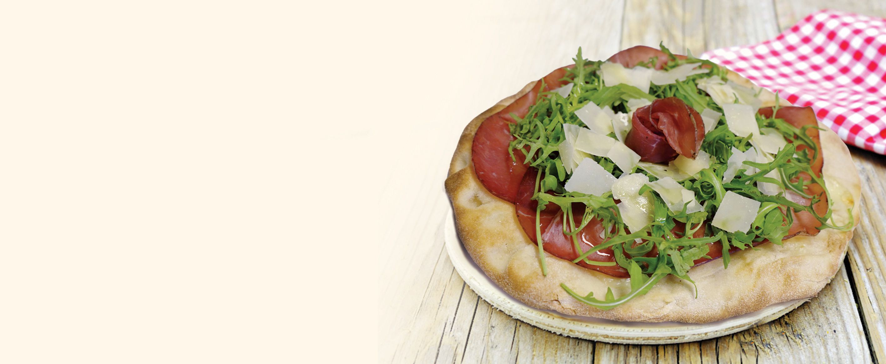 Pizza tonda con rucola, scaglie di parmigiano e bresaola arrotolata al centro, su tovagliolo a quadretti rossi e bianchi