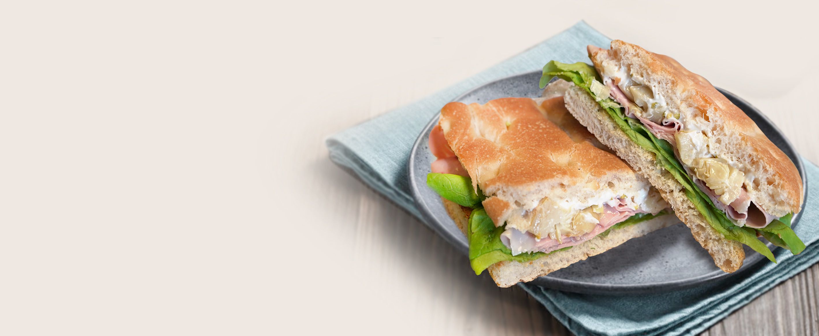 Panino di focaccia tagliato a metà, farcito con prosciutto, insalata e formaggio spalmabile, su un piatto