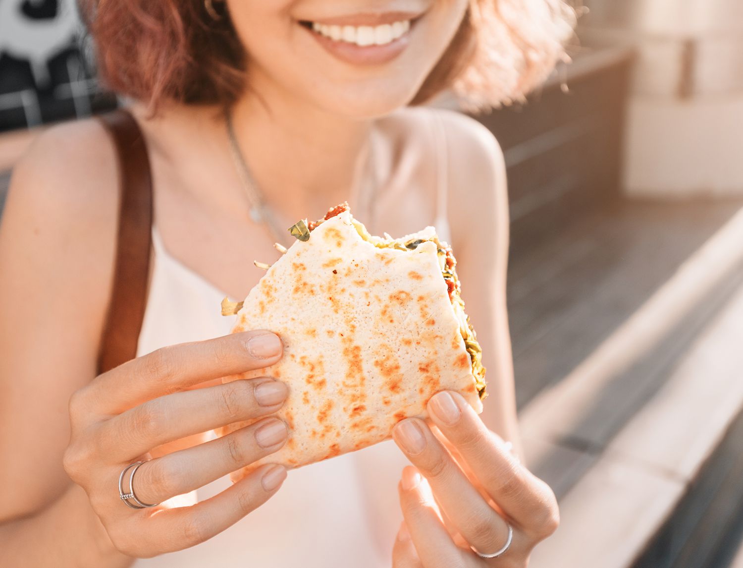 Primo piano di una persona sorridente che morde una piadina ripiegata farcita, tenuta con entrambe le mani