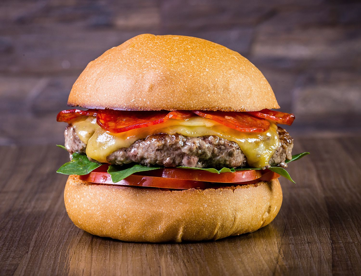 Hamburger con formaggio fuso e peperoni grigliati a fette, fotografato frontalmente su un tavolo di legno scuro