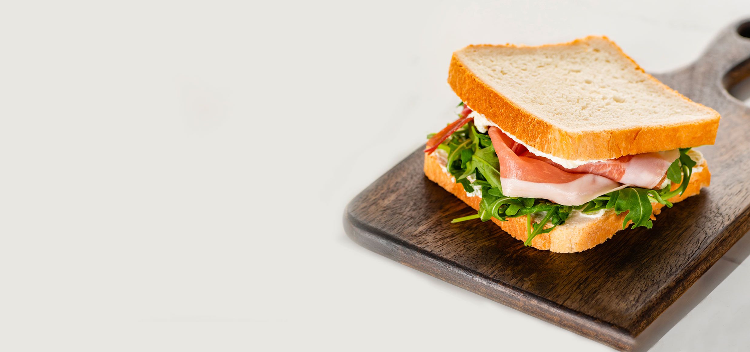 Panino con prosciutto crudo e rucola tra due fette di pane bianco, su un tagliere di legno scuro