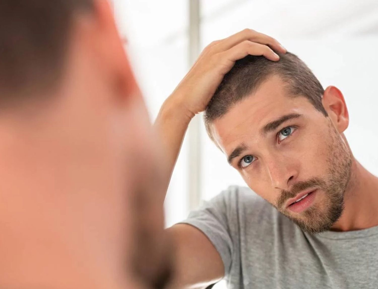 Uomo allo specchio che si tocca i capelli corti con espressione preoccupata